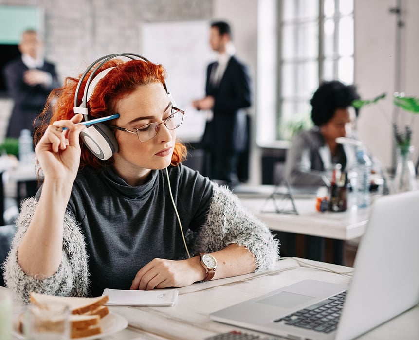 young-female-entrepreneur-using-laptop-thinking-about-email-she-has-received-while-listening-music-headphones-work-there-are-people-background